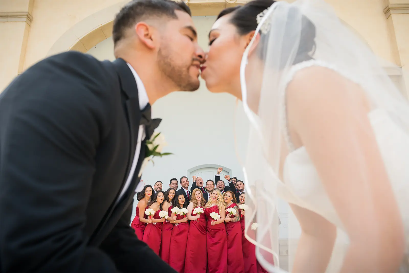 couple kissing with wedding party behind